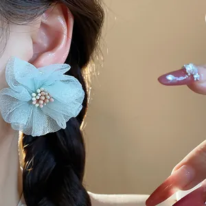 Dettaglio di eleganti orecchini a lobo con fiori in chiffon verde menta indossati sul lobo.
