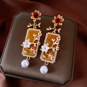 Dettaglio di orecchini vintage con rose rosse, rami fioriti e pendenti di perle