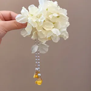Detailed view of large off-white fabric flower hair clip with dangling pearl tassels.