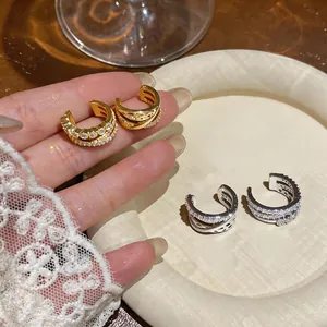 Detalle de pendientes ear cuff de triple capa cruzada con circonitas en oro y plata