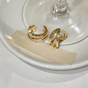 Primer plano de ear cuffs dorados con circonitas y diseño cruzado sobre fondo blanco.