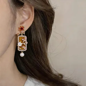 Primo piano di orecchini rettangolari vintage con fiori e perle indossati.