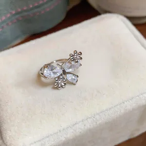 Detail of a delicate silver-toned ring featuring a zircon butterfly and metal flowers.