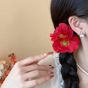 Gros plan d'une pince à cheveux fleurie en tissu rouge vif portée élégamment sur une tresse