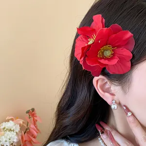 Détail d'une grande pince à cheveux fleur en tissu rouge sur cheveux sombres