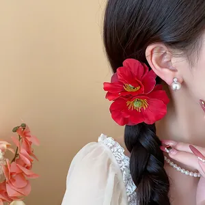 Détail d'une pince à cheveux fleur rouge en tissu sur une coiffure tressée pour femme
