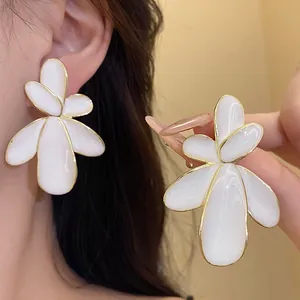 Close-up of white enamel flower stud earrings with gold plating and silver needles