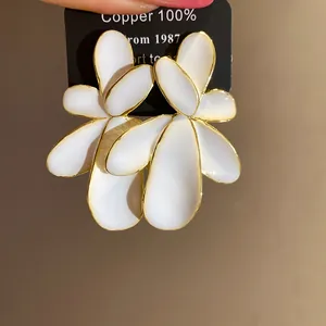 Detailed macro shot of elegant white oil-drop flower earrings with gold plated edges on card