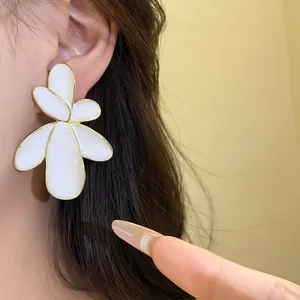 Detailed close-up of a large white enamel flower earring with gold edges on a model's ear