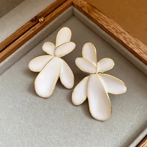 Detailed view of elegant white enamel flower stud earrings with gold edges in a box