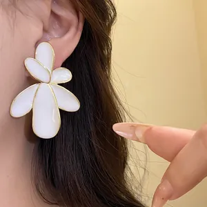 Close-up of elegant white enamel flower stud earrings with gold trim on ear