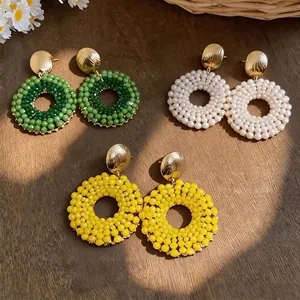 Elegant handmade beaded circular drop earrings in green white and yellow on wooden table