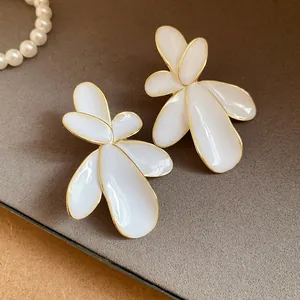 Close-up of white flower-shaped earrings with gold edges and enamel finish.