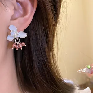 Close-up of elegant white enamel flower earrings with pink pearl charms worn on ear.
