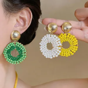 Detailed macro view of handmade beaded hoop earrings in vibrant green, white and yellow.