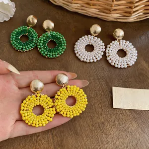 Close-up of hand holding yellow beaded hoop earrings with green and white pairs