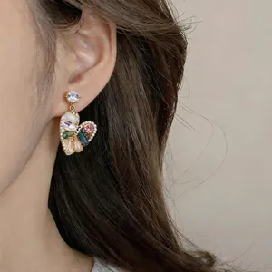Close-up detail of a vintage heart-shaped earring with multi-colored stones on a model.