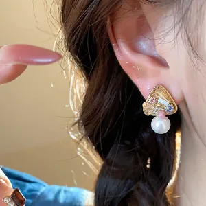 Detail view of an elegant 18k gold plated geometric pearl stud earring being worn on an ear