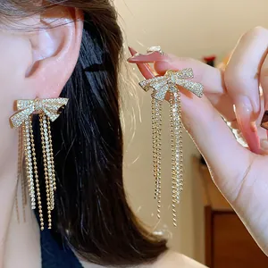 Detail view of gold-plated bow earrings with zircon stones and long tassel drop design