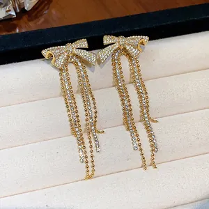 Close-up of gold-plated bow earrings with sparkling zircon tassels in jewelry box.