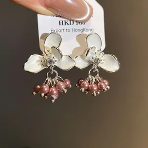 Close-up of elegant white enamel flower stud earrings with dangling pink pearls