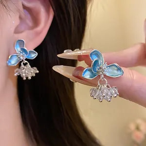 Detail showing elegant light blue enamel flower earrings with dangling clear beads.