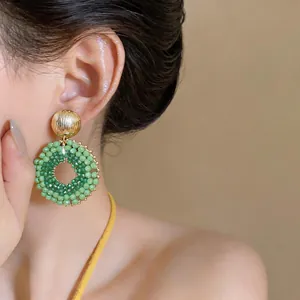 Macro view of green handmade beaded circular drop earrings worn on model's ear