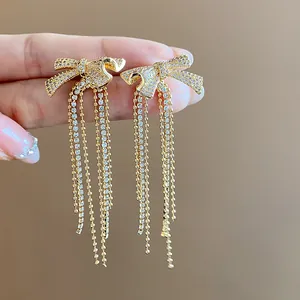 Macro view of 18k gold-plated bow tassel earrings with sparkling zircon stones held by hand.