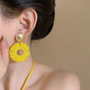 Detail shot of vibrant yellow beaded circular earrings with a gold stud on a model
