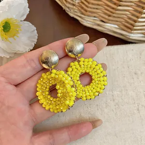 Close-up of vibrant yellow beaded round earrings with textured gold studs