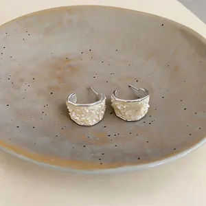 Close-up of C-shaped earrings featuring textured crushed shell inlay and silver finish