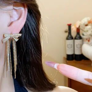 Close-up of 18k gold-plated bow earrings with sparkling zircon tassels on model.