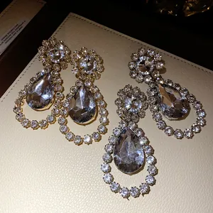 Detailed macro view of elegant crystal-encrusted waterdrop drop earrings on beige leather.