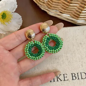 Detail view of circular earrings with green beads and gold textured metal stud on hand.
