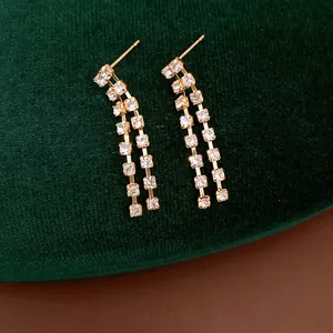 Detailed view of elegant gold rhinestone tassel earrings on green velvet background.