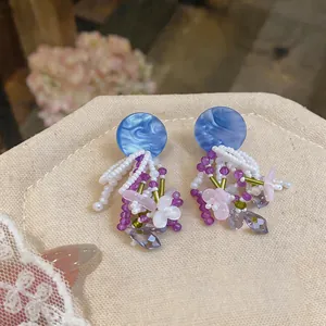 Detailed close-up of handmade beaded earrings with blue marble discs and pink flowers