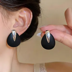 Close-up of elegant black matte teardrop earrings with silver metallic accent worn on ear