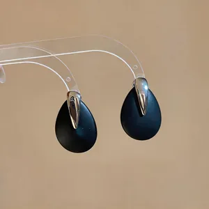 Close-up of minimalist black matte droplet earrings with silver metallic accents
