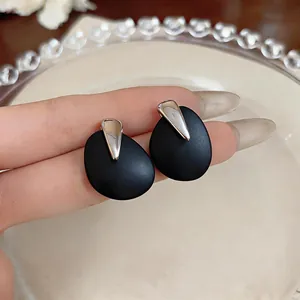 Close-up of minimalist matte black teardrop earrings with silver metal detail