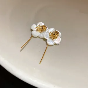 Close-up of 18k gold plated shell flower drop earrings with intricate gold filigree center.