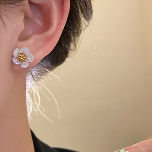 Detailed macro view of white shell flower earring with 18k gold plating on model's ear