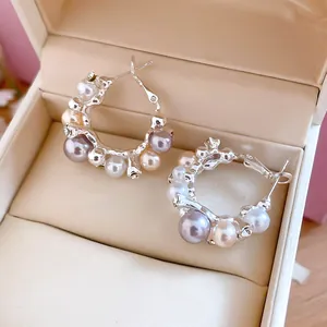 Vue détaillée de boucles d'oreilles créoles avec perles et zircons dans une boîte à bijoux.