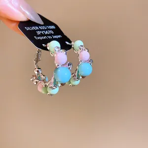 Gros plan de boucles d'oreilles créoles avec des perles pastel et des oxydes de zirconium.