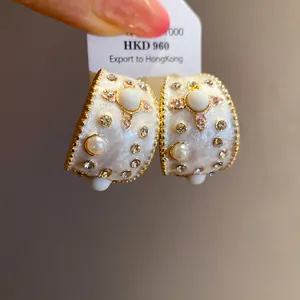 Dettaglio di orecchini vintage a forma di C con smalto bianco, perle e piccoli strass