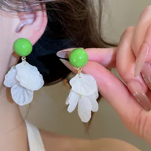 Détail rapproché montrant les clous ronds verts et les pompons en nacre blanche des boucles.