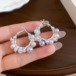 Détail de boucles d'oreilles créoles avec perles mauves et blanches tenues à la main