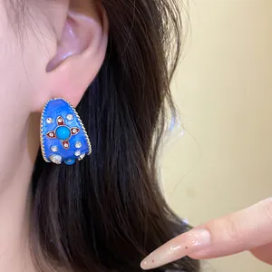 Primo piano di un orecchino vintage in smalto blu a forma di C con strass sull'orecchio.