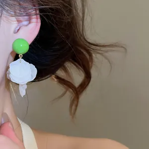 Détail rapproché de boucles d'oreilles boules vertes avec pétales de coquillages blancs