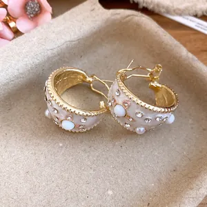 Macro dettagli di orecchini a cerchio a C vintage con perle, strass e smalto crema
