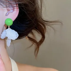 Gros plan de boucles d'oreilles rondes vertes avec pampilles de pétales blancs pour l'été.